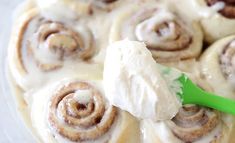 a green spatula being used to dip cinnamon rolls