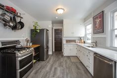 a kitchen with white cabinets and stainless steel appliances, including an oven, refrigerator, dishwasher, stove top and sink