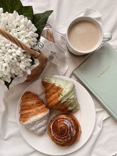 a white plate topped with pastries next to a cup of coffee and a book