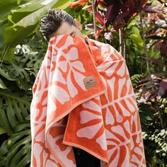 a man wrapped up in an orange and white patterned towel with his eyes closed while standing next to some tropical plants