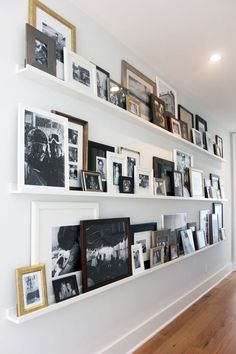 a wall filled with lots of pictures and framed photos next to a wooden floor in front of a white wall