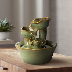 a green bowl sitting on top of a wooden table next to a potted plant