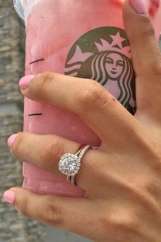 a woman's hand holding a starbucks cup with a diamond ring on it and a pink drink in the background