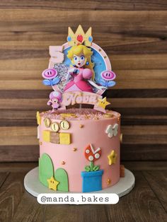 a pink cake decorated with mario and princess peaches on top of a wooden table