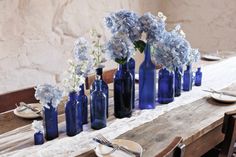 there are many blue vases with flowers in them on the table, along with plates and utensils