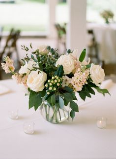 a vase filled with white flowers sitting on top of a table next to glasses and candles