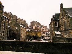 an old city with snow on the ground and buildings in the background, as seen from behind a stone wall