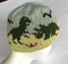 a white mannequin head wearing a green and yellow knitted hat with dinosaurs on it