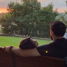 a man and woman sitting on a bench looking out at the grass in front of them