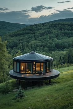 a round house in the middle of a grassy field with trees and mountains behind it