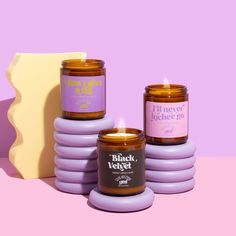 three candles sitting next to each other on top of a pink surface with purple and yellow accents