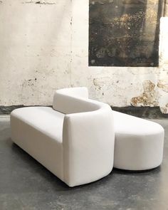 a white couch sitting on top of a cement floor next to a wall with a painting hanging above it