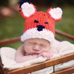 a baby wearing a red and white knitted bear hat while laying in a wooden crate