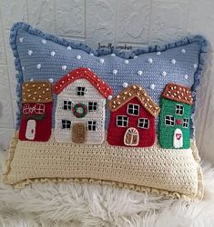 a crocheted pillow with houses on it sitting on a white furnishing