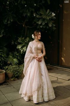 a woman in a pink and gold wedding gown standing on the sidewalk with greenery behind her