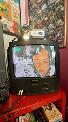 an old tv sitting on top of a red table next to a book shelf with books