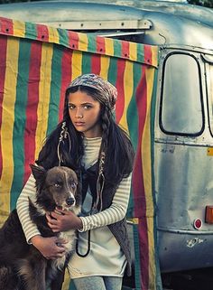 a woman is holding a dog in front of a van with a striped tent behind her