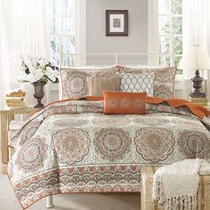 an orange and white comforter set with pillows on the bed in front of a window