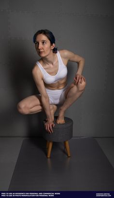 a woman sitting on top of a stool with her legs crossed and hands behind her back