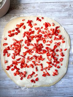 an uncooked pizza topped with strawberries on top of a wooden table next to a bowl