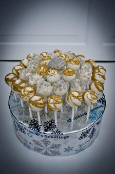 cake pops with gold and white frosting are arranged in a decorative box on a table