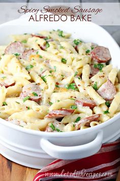 a white bowl filled with pasta and sausage on top of a wooden table next to a red striped napkin