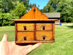 a hand holding a small wooden drawer in the grass