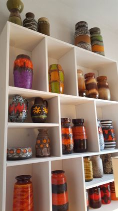 a shelf filled with lots of colorful vases on top of white shelving units