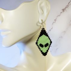 a pair of earrings with an alien face on it, hanging from a mannequin head