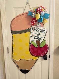 a welcome to class sign hanging on the front door with an apple and pencil in it