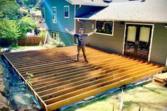 a man standing on top of a wooden deck in front of a blue house with his arms outstretched