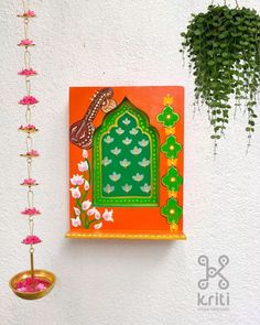 an orange and green painting hanging on the side of a white wall next to plants