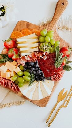 an assortment of cheeses, fruits and meats on a wooden platter with utensils