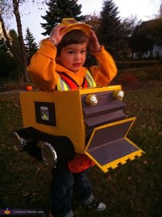 a young boy dressed up as a construction worker holding a cardboard box in his hands