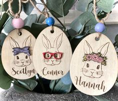 three wooden tags with bunny ears and glasses on them, hanging from a tree branch