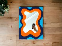 a hand holding a cell phone in front of a mirror on top of a wooden floor