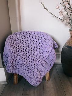 a purple crocheted blanket sitting on top of a wooden stool next to a vase