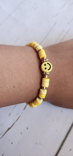 a woman's arm wearing a yellow bracelet with smiley face beads