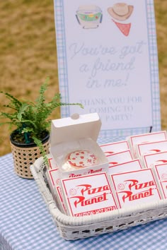 some pizza boxes sitting on top of a blue and white checkered table cloth with a sign in the background