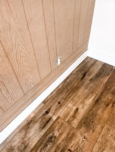 a wood floor in a kitchen with white trim on the wall and wooden cabinet doors