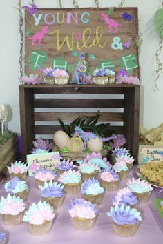 a table topped with cupcakes covered in frosting next to a wooden sign