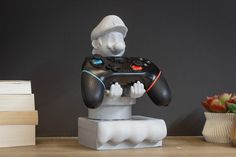 a white robot holding a black controller on top of a table next to some books