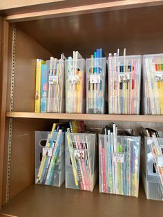 several clear bins with pens and pencils in them sitting on a wooden shelf