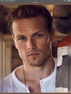 a man is looking at the camera while wearing a white t - shirt and necklace