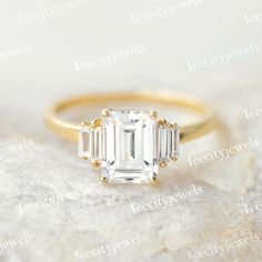 an emerald cut diamond ring with three baguettes in yellow gold on top of a rock