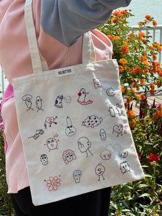 a woman carrying a tote bag with cartoon drawings on it and flowers in the background