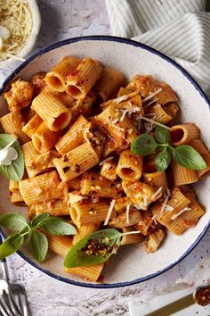 a bowl filled with pasta and sauce on top of a white table next to silverware