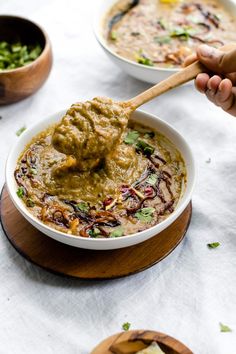 a bowl of soup with a wooden spoon in it and two bowls full of food on the table