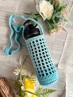 a crocheted water bottle cover sitting on top of an open book next to flowers