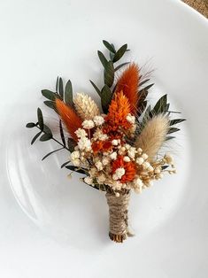 an arrangement of dried flowers on a white plate with greenery and leaves in the center